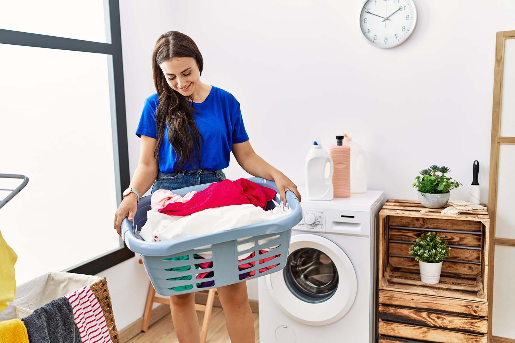 A woman carrying a laundry basket in a laundry room.